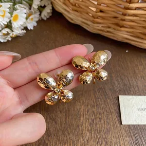 Elegant handheld gold hammered butterfly-shaped stud earrings in a warm floral setting