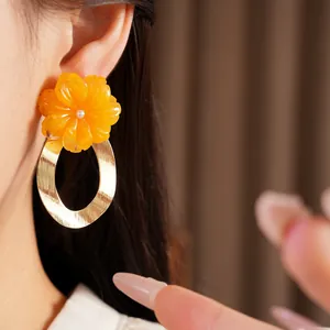 Macro view of bright orange resin flower earrings with large golden oval hoops