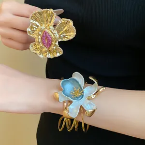 Detailed view of vintage gold floral cuff and blue enamel flower bracelet on wrist.
