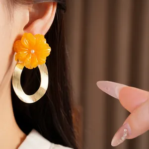 Close-up detail of a person wearing an orange resin flower earring with a gold metal hoop