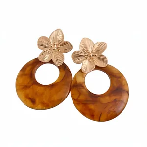 Elegant golden metal flower and marbled brown resin hoop earrings on white background