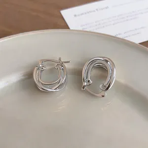 Detailed macro shot of silver crossover double-layer hoop earrings resting on a ceramic dish