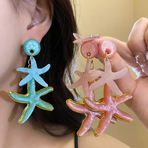 Detailed shot of shimmering resin starfish drop earrings in cyan and pink finishes