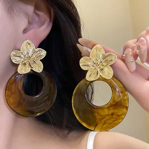 Detailed macro view of elegant gold metal flower and amber resin hoop earrings on a model