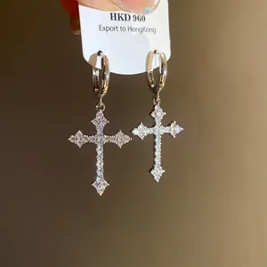 Macro detail of sparkling zircon-encrusted cross pendant earrings in silver finish