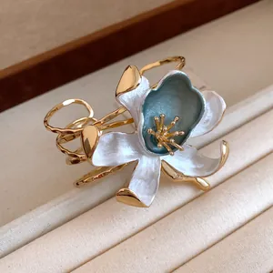 Macro view of vintage gold bangle featuring a white and blue pleated enamel flower.