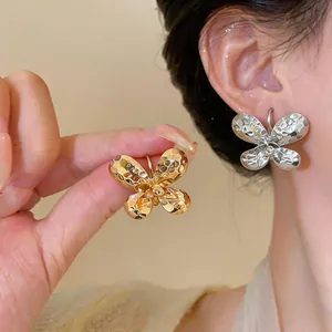 Macro view of textured metallic butterfly C-shaped earrings in gold and silver finishes