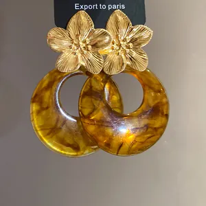 Detail of golden metal flower earrings with marbled amber resin round pendants