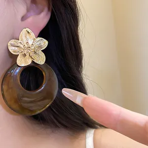 Detailed view of elegant gold metal flower and brown resin circular drop earrings on a model