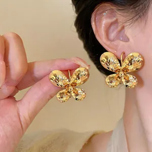 Detail of gold butterfly earrings with hammered texture shown on ear and held by hand