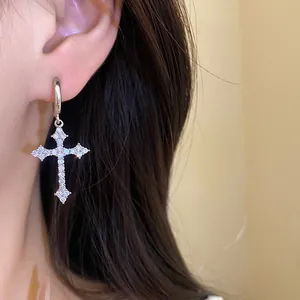 Close-up detail of silver zircon cross pendant hoop earring worn on an ear.