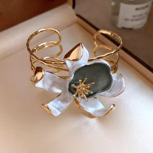 Detailed view of a vintage gold cuff bracelet with a large white enamel flower.