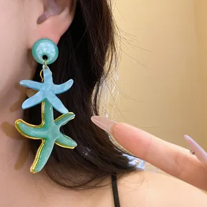 Close-up of stylish vacation-style blue and green resin starfish pendant earrings on ear.