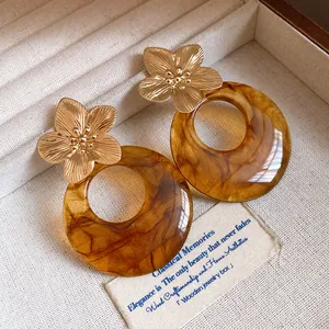 Close-up of elegant amber resin earrings with golden metal flower studs on a fabric tray.