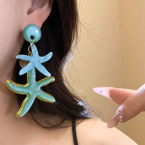 Close-up of oversized blue and teal starfish resin drop earrings on a model's ear