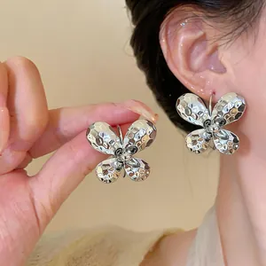 Close-up of silver butterfly C-shaped earrings with hammered metal texture on ear