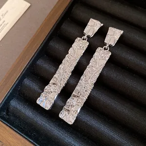 Close-up of silver wrinkled rectangle drop earrings with metallic texture on black tray
