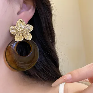 Detailed view of golden flower stud with brown translucent resin hoop earring on ear