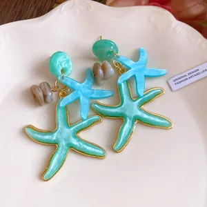 Detailed view of teal resin starfish dangle earrings on a decorative plate.