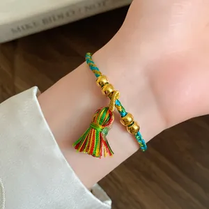 Close-up of handmade colorful cord bracelet with gold beads and tassel detail