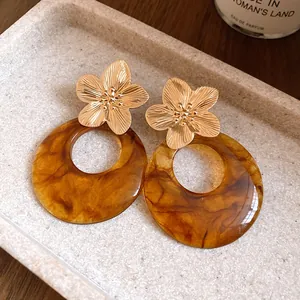 Close-up detail of gold metal flower stud earrings with amber resin hoop pendants.