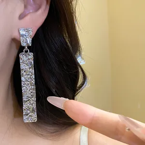 Close-up detail of textured silver rectangular drop earrings with a luxurious finish