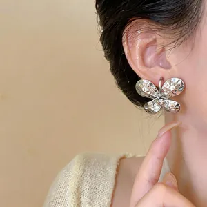 Detailed view of a silver hammered butterfly C-shaped stud earring on a model's ear