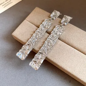 Close-up detail of textured rectangular silver-tone drop earrings with crumpled finish