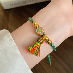 Close-up of a hand-woven colorful rope bracelet with gold beads and a tassel detail.