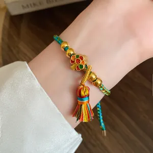 Close-up view of a hand-woven colorful rope bracelet with tassel and gold beads