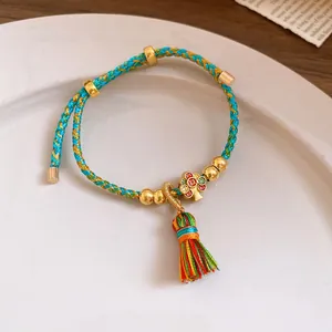 Close-up of handmade woven colorful rope bracelet featuring a vibrant tassel and gold charms