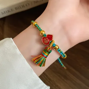 Close-up detail of a handmade woven five-color cord bracelet with a gold Fu charm and tassel