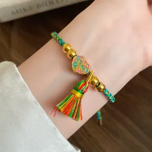 Detail view of a handmade woven five-color cord bracelet with gold beads and tassel