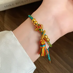 Close-up of a hand-woven five-color rope bracelet featuring gold beads and a colorful tassel