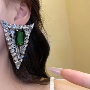 Detail of luxury triangular silver stud earring with a green emerald stone and rhinestones
