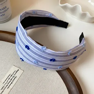 Dettaglio di cerchietto in tessuto a righe blu e bianche con divertenti pompon blu.