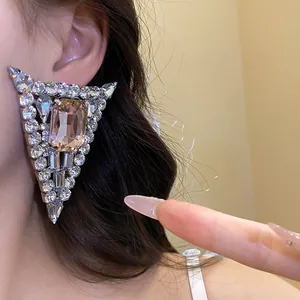 Close-up of a glamorous triangular rhinestone earring featuring a large champagne gemstone.