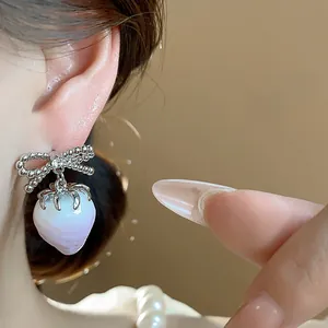 Close-up detail of cute pink resin strawberry ear studs with shiny zircon bowknot design