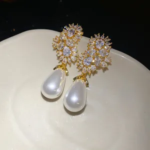 Primer plano de elegantes pendientes colgantes dorados con circonitas y perlas de lágrima