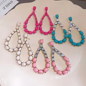 Dettaglio di orecchini pendenti a goccia colorati con pietre finte e cristalli.