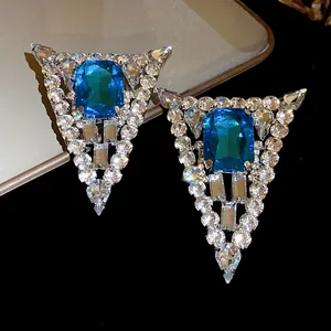 Macro detail of triangle stud earrings with vibrant blue gemstone and clear crystals