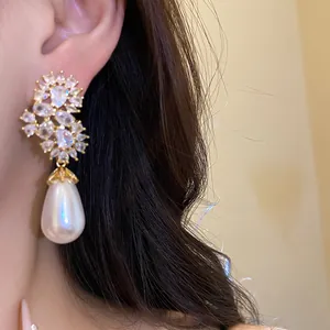 Primer plano de elegantes pendientes dorados con flores de circón y perlas de gota blancas