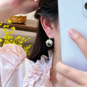 Close-up of sweet ice-clear crystal ball earrings with small enamel flowers on a model