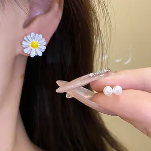 Detailed view of daisy stud earring worn on ear and pearl studs held by hand