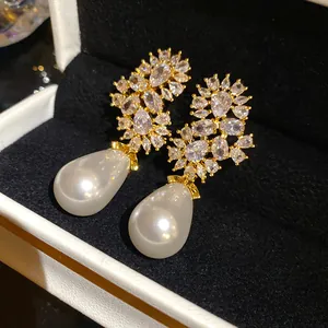 Vista detallada de elegantes pendientes colgantes dorados con circonitas y perlas