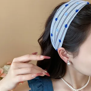 Dettaglio di una fascia per capelli in tessuto a righe blu con ricamo floreale su modella.