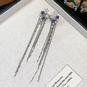 Close-up of zircon star tassel ear clips with purple and clear stones in a gift box.