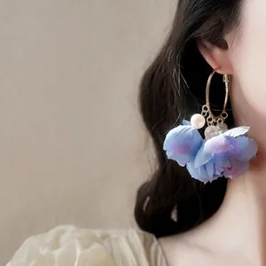 Vue détaillée d'une élégante boucle d'oreille fleur en tissu bleu avec perles sur modèle