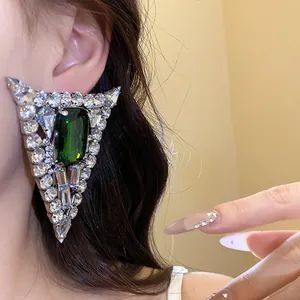 Close-up of triangle rhinestone earrings with a green emerald-cut gemstone detail.