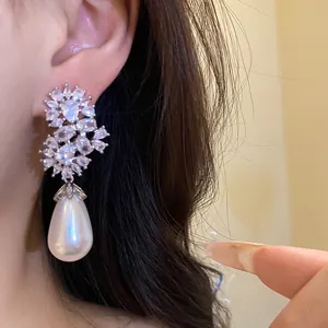 Detalle de elegantes pendientes de circonitas con una gran perla en forma de gota en la oreja.